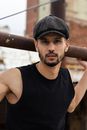 Stylish man poses confidently in black tank top and cap outdoors.